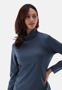 Langärmliges Turtleneck-Top aus dunkelblauem Stoff mit einer glatten Textur, ausgestattet mit einem Schalkragen und einer taillierten Silhouette, die stilvolle Nähedetails aufweist.