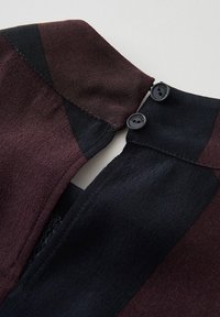 Dunkelrot-braunes und schwarzes Gewebe mit glatter Textur, das einen Kragen und zwei schwarze Knöpfe am Halsausschnitt aufweist.