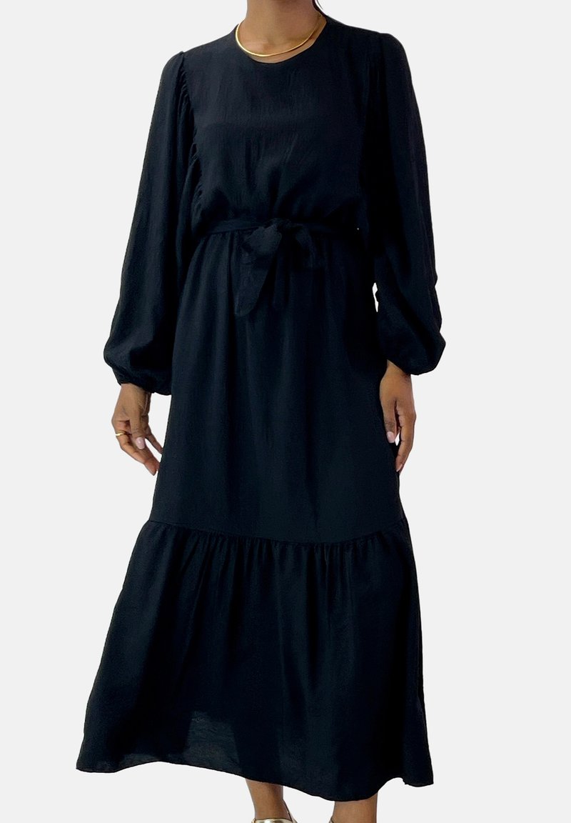 Vestido negro de manga larga con escote redondo, cinturón de cintura ceñido y falda de volantes. Hecho de una tela ligera con textura fluida.