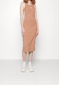 Ribbade, ärmlösa midiklänning i ljusbrunt med vita sidostrekar och logodetalj. Bärs med vita chunky sneakers. Slät tygtextur.