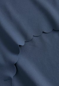 Granatowy materiał z falbanką, gładką teksturą i jednolitym wzorem. Materiał wydaje się elastyczny i lekki.