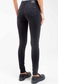 Jeans skinnies negros de mezclilla, con una cintura alta y dos bolsillos en la parte trasera. Llevados con zapatos de plataforma negros. Fondo liso.