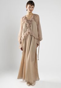 Helles beige langes Kleid mit Rüschendetails, langen Ärmeln und einer weichen, durchsichtigen Textur. Bänder in der Taille und an den Manschetten betonen die Designdetails.