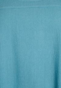 Tessuto azzurro chiaro con un delicato motivo a diamante strutturato e una cucitura orizzontale impunturata vicino alla parte superiore.
