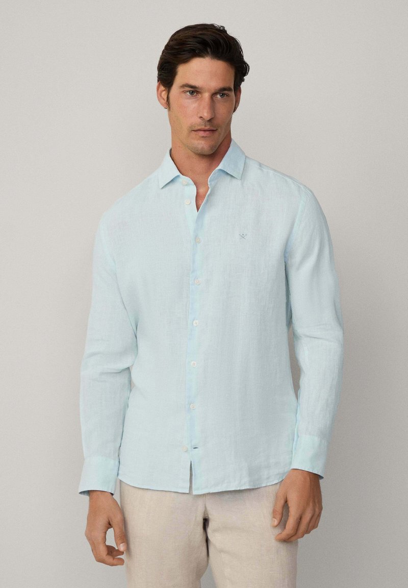 Light blue long-sleeve shirt made from a textured fabric, featuring a button-down front and a subtle embroidered emblem on the chest.