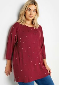 Burgundy tunika med trekvartsärmar och silverstjärnor som dekoration. Mjuk tyg, avslappnad passform, sidofickor och rund halsringning.