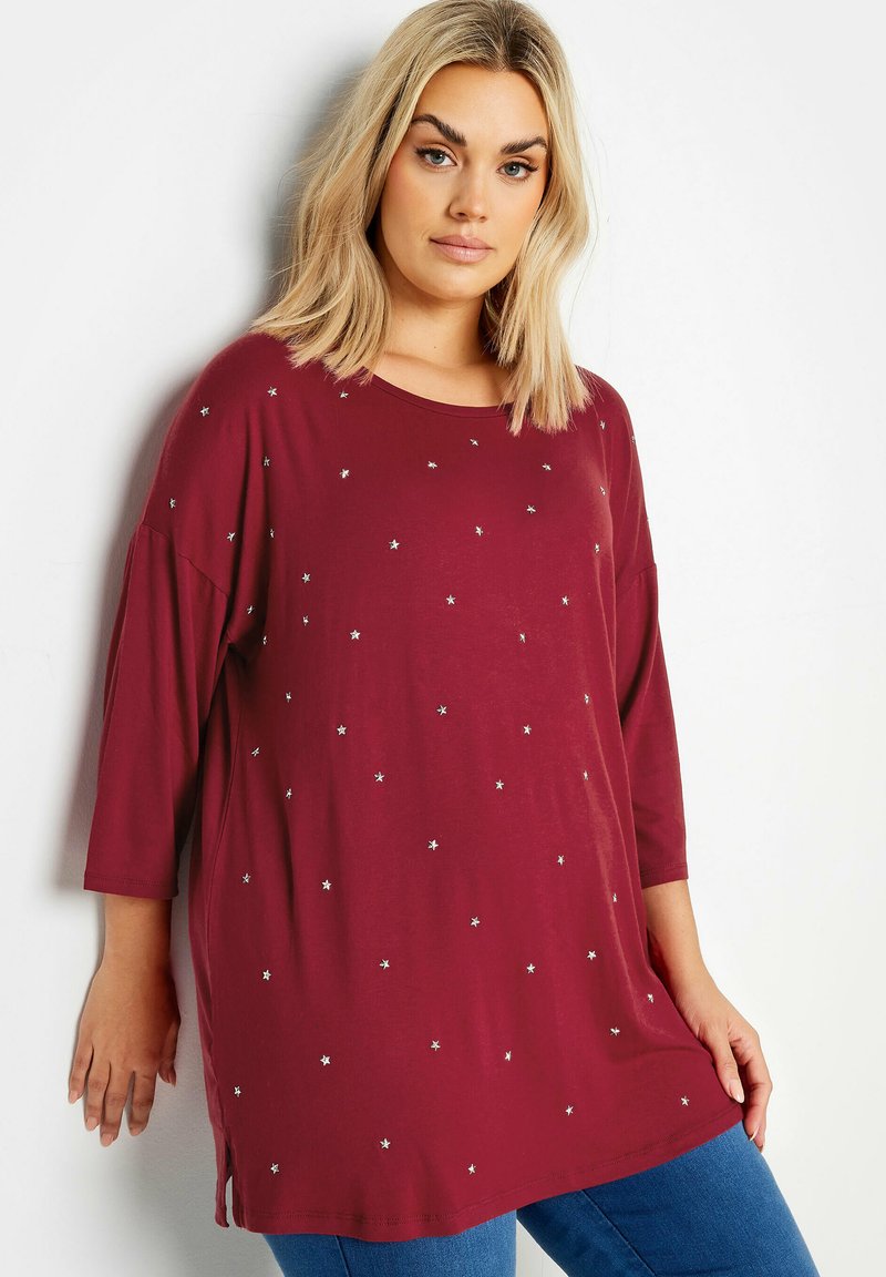 Burgundy tunika med trekvartsärmar och silverstjärnor som dekoration. Mjuk tyg, avslappnad passform, sidofickor och rund halsringning.