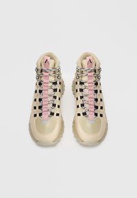 Botas de senderismo beige con suelas gruesas, lazos cuadrados de color negro, cordones grises y negros, y lengüetas de tiro rosas sobre un fondo blanco.