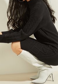 Schwarzes Strickkleid mit Zopfmuster, kombiniert mit hellgrauen, patentierten, krokodilgeprägten, kniehohen Stiletto-Stiefeln.