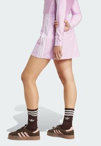 Skort atlético rosa con rayas blancas a los lados, combinado con zapatillas marrones con acentos rosas y calcetines oscuros a rayas.