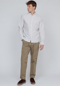 Leicht gestreiftes Button-Down-Hemd in Weiß und Grau, kombiniert mit beigen Hosen und dunkelbraunen Schuhen. Die Passform ist lässig und entspannt.