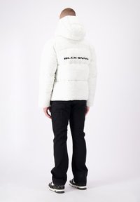 Witte pufferjack met capuchon en quilting, met het "BLCK BNNS" logo op de achterkant. Gemaakt met zwarte broek en kleurrijke schoenen.