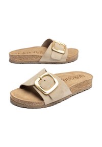 Des sandales beige à enfiler avec une large sangle, dotées d'une grande boucle en métal doré. Semelle en liège avec un lit de pied texturé pour le confort.