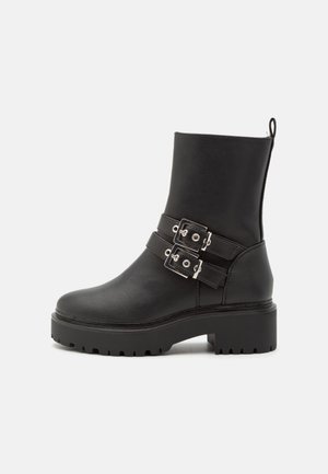 Black ankle boot made of leather featuring two silver buckle straps, a chunky sole, and a textured upper with a pull tab at the back.