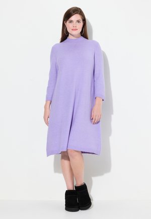 Lavendelfarbenes Wollmischkleid mit hohem Kragen, Dreiviertelärmeln und einer lockeren Silhouette, kombiniert mit schwarzen Stiefeletten.