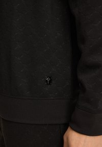 Felpa nera con un motivo testurizzato, polsini a coste e un piccolo logo lucido vicino all'orlo. Tessuto morbido con un design aderente.