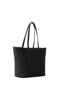 Sac tote en cuir noir avec une surface texturée, deux poignées et un accent en forme de logo circulaire. Forme rectangulaire avec des coutures décoratives.