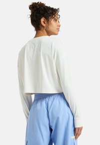 Lyhytlyhyt paita off-white-värissä, pehmeästä kankaasta ja pyöreällä kaula-aukolla. Yhdistetty vaaleansinisiin, kevyisiin, elastisilla vyötärönauhoilla varustettuihin housuihin.