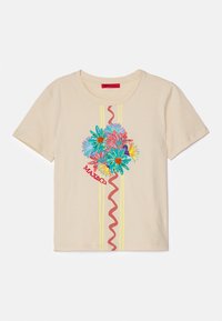 Camiseta de color crema con bordado floral colorido y un logo rojo. El diseño incluye dos franjas amarillas y una línea roja ondulada.