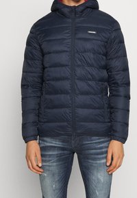 Navy puffer jacket with a hood, zippered front, and elastic cuffs. Features horizontal stitch pattern and a small brand logo on the chest.