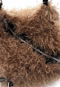 Brązowa, kręcona torebka z futerka ekologicznego z srebrnym zamkiem błyskawicznym i czarnymi skórzanymi akcentami na białym tle.