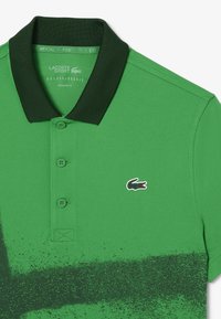 Grön polo t-shirt i texturerat tyg, med en mörkgrön krage, tre knappar och en liten broderad krokodil-logga.