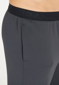 Dunkelgraue Sporthosen bestehen aus einem strukturierten Rippstoff, haben einen breiten elastischen Bund und eine seitliche Tasche für Funktionalität.