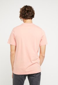 T-shirt de manga corta en color rosa con un corte relajado, fabricada en algodón suave. Presenta un diseño minimalista con cuello redondo y sin patrones visibles.