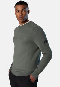 Maglione in tessuto verde spento con una finitura texturizzata. Presenta un collo rotondo, maniche lunghe e un logo sul fronte. Polsini e orlo a coste.