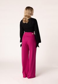 Zwarte cropped top met lange mouwen, gecombineerd met hooggewaste, wijde roze broek met een uitsnede detail in de taille.