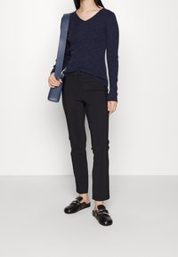 Pull marin en maille à manches longues et col en V, pantalon noir ajusté, et sabots noirs avec accents métalliques argentés. Texture lisse, silhouette élancée.