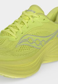 Φωτεινό κίτρινο παπούτσι τρεξίματος Saucony με πλεκτό επάνω μέρος, παχιά σόλα και αντανακλαστικό λογότυπο στο πλάι, σε κλίση ώστε να φαίνονται τα κορδόνια και η περιοχή των δακτύλων.