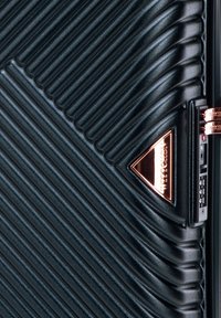 Valigia nera con texture a righe verticali, hardware color oro rosa e logo a triangolo. Presenta una combinazione di lucchetto sul lato.