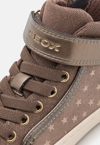Sneaker alta marrone con motivo a stelle, tomaia in tessuto, occhielli con accenti dorati e una fascia metallica etichettata "GEOX". Suola in gomma.