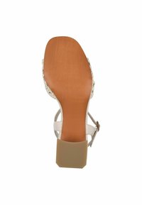 Sandale blanche avec une tige tissée, une semelle texturée marron et un talon beige de forme carrée. La bride de cheville est dotée une boucle en métal.