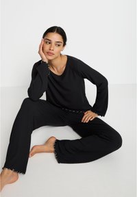 Ensemble de détente noir à côtes comprenant un haut à manches longues avec un décolleté en scoop et un pantalon avec des ourlets en scallop. Tissu confortable et coupe décontractée.