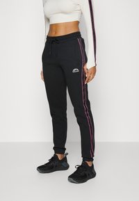 Pantalones de sudadera negros con rayas laterales rosas, cintura elástica y tobillos ajustados. Tela suave con un detalle de logo en la cadera.