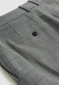 Tela de cuadros en blanco y negro con un primer plano de un bolsillo con solapa asegurado por un botón negro en una prenda.