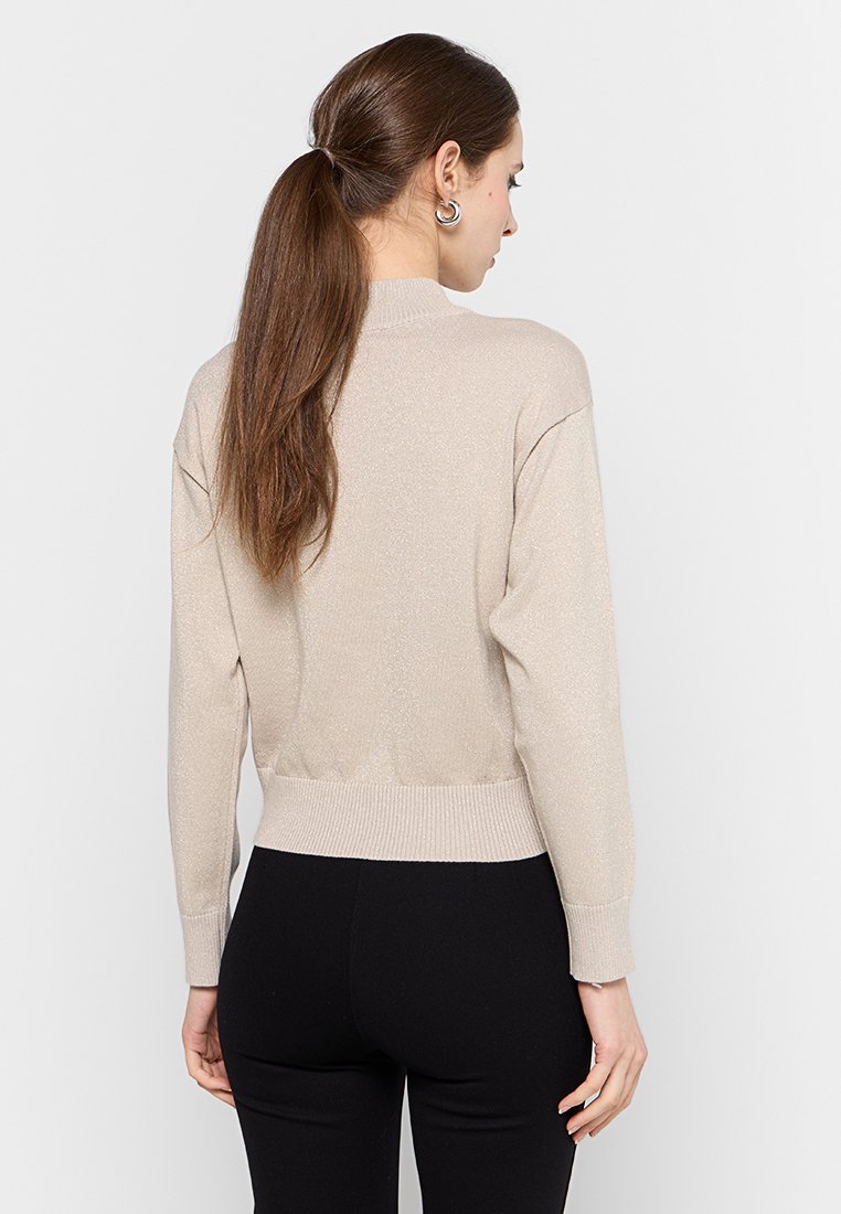 Maglione corto beige con una leggera lucentezza, orlo a costine e maniche ampie. Il materiale sembra morbido e leggermente leggero.