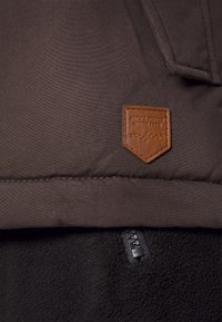 Dark brown outer fabric with a textured fleece lining, featuring a brown leather logo patch and a black zipper detail.