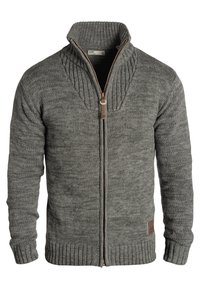 Grijze trui met rits en hoge kraag, geribbelde manchetten en zoom. Heeft een gestructureerd patroon en een bruin leren logoplaatje aan de zijkant.