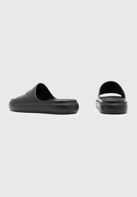 Sandale din spumă neagră, cu deschidere la spate, textură netedă, talpă groasă și branding subtil pe partea superioară. Design elegant și minimalist.