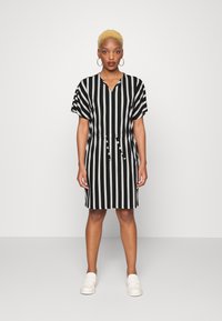 Vestido às riscas preto e branco com decote em V, mangas curtas, cintura com cordão e comprimento até ao joelho, combinado com mocassins de cores claras.