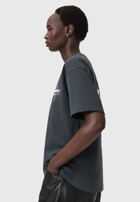 Tummanharmaa puuvillainen t-paita, jossa lyhyet hihat, rento istuvuus ja pyöreä pääntie. Edessä painetut yksityiskohdat.