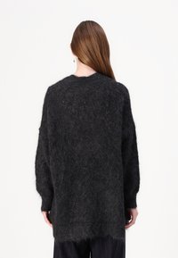 Overdimensjonert svart mohair-genser med en fuzzy tekstur. Løs passform, rund hals, lange ermer og ujevn kant. Minimalistisk design.