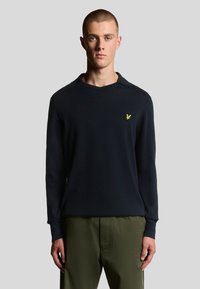 Maglione blu navy a maglia con scollo a V e maniche lunghe, caratterizzato da un piccolo logo giallo sul lato sinistro del petto. Realizzato in tessuto morbido.