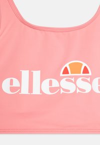Svetloružový športový podprsenka so širokým bielym logom "ellesse" a slnečným grafickým vzorom v oranžovej a žltej farbe. Hladká textura s okrúhlym výstrihom.