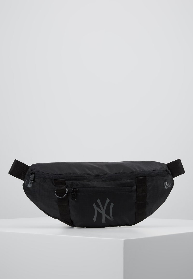 Sac en nylon noir de forme arrondie, avec une poche zippée à l'avant et le logo des New York Yankees en gris subtil. Bandoulière ajustable.