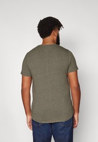 Olivno zeleni kratki rokav t-shirt iz teksturiranega materiala, z okroglim izrezom in ravnim zadnjim šivom. V kombinaciji s temnimi kavbojkami.