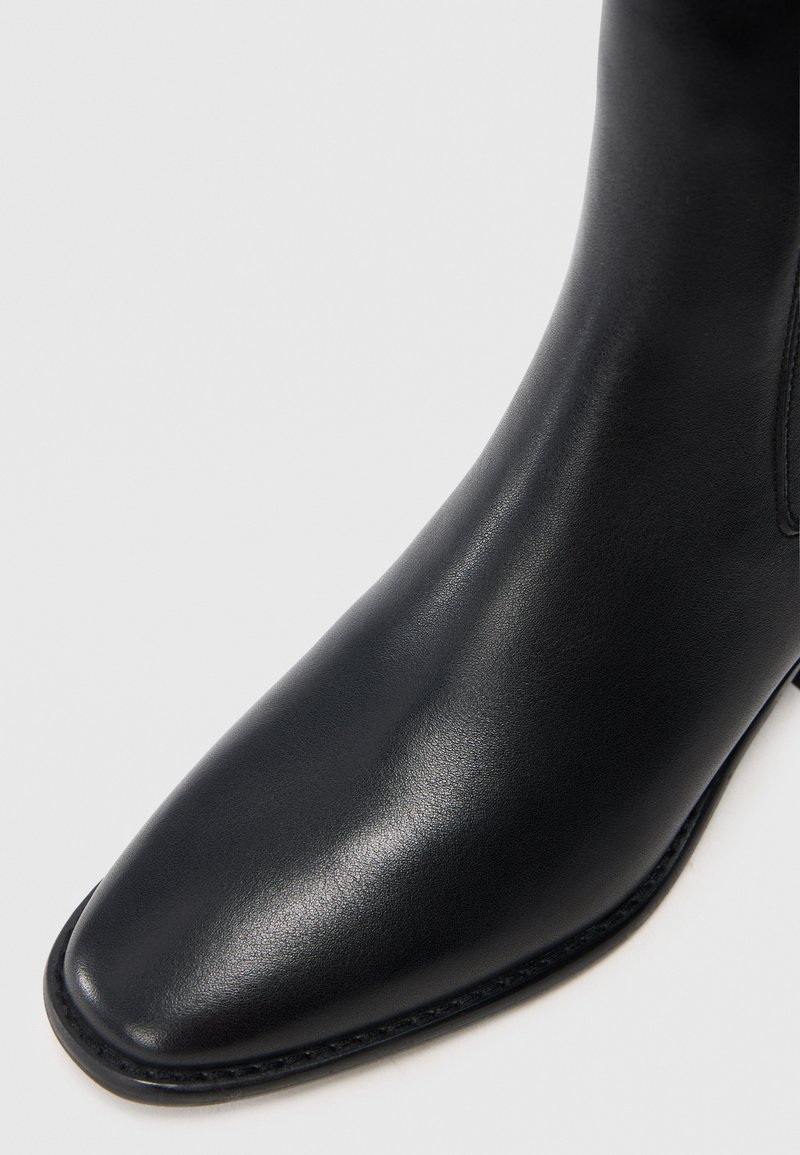 Schwarze Leder-Stiefelette mit rechteckiger Spitze, glatter Textur und minimaler Naht. Verfügt über ein elegantes Design und einen niedrigen Absatz.